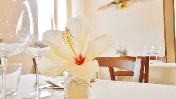 Un tavolo da pranzo con una tovaglia bianca, un vaso di vetro con un fiore bianco e bicchieri da vino vuoti.