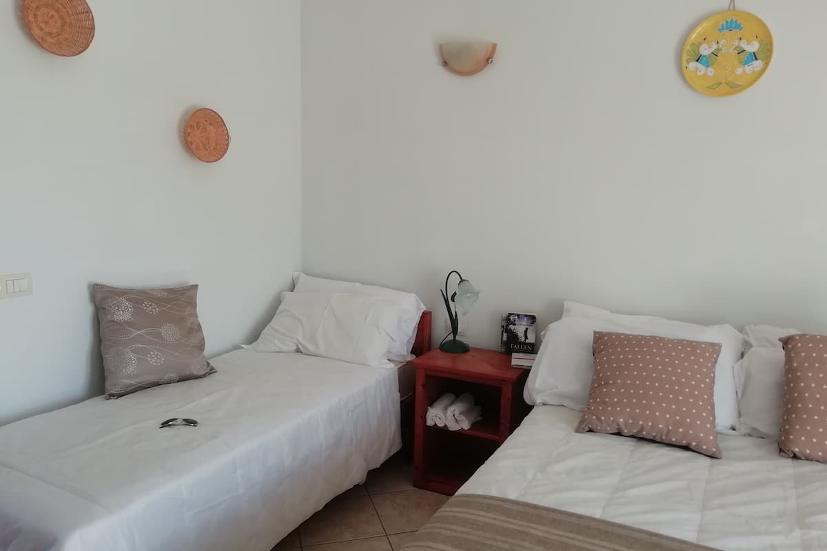 A bedroom with two single beds, a nightstand with a lamp, and decorative wall hangings.