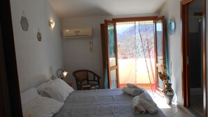 A bedroom with a bed, a chair, a potted plant, and a view through a glass door. - Hotel VelaSole (Siniscola)