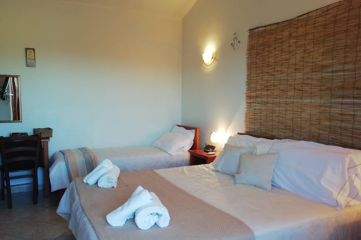 A hotel room with two beds, a desk with a chair, a lamp, and a large window with blinds.