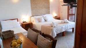 A hotel room with two beds, a wooden table with a basket of lemons, and a TV mounted on the wall. - Hotel VelaSole (Siniscola)