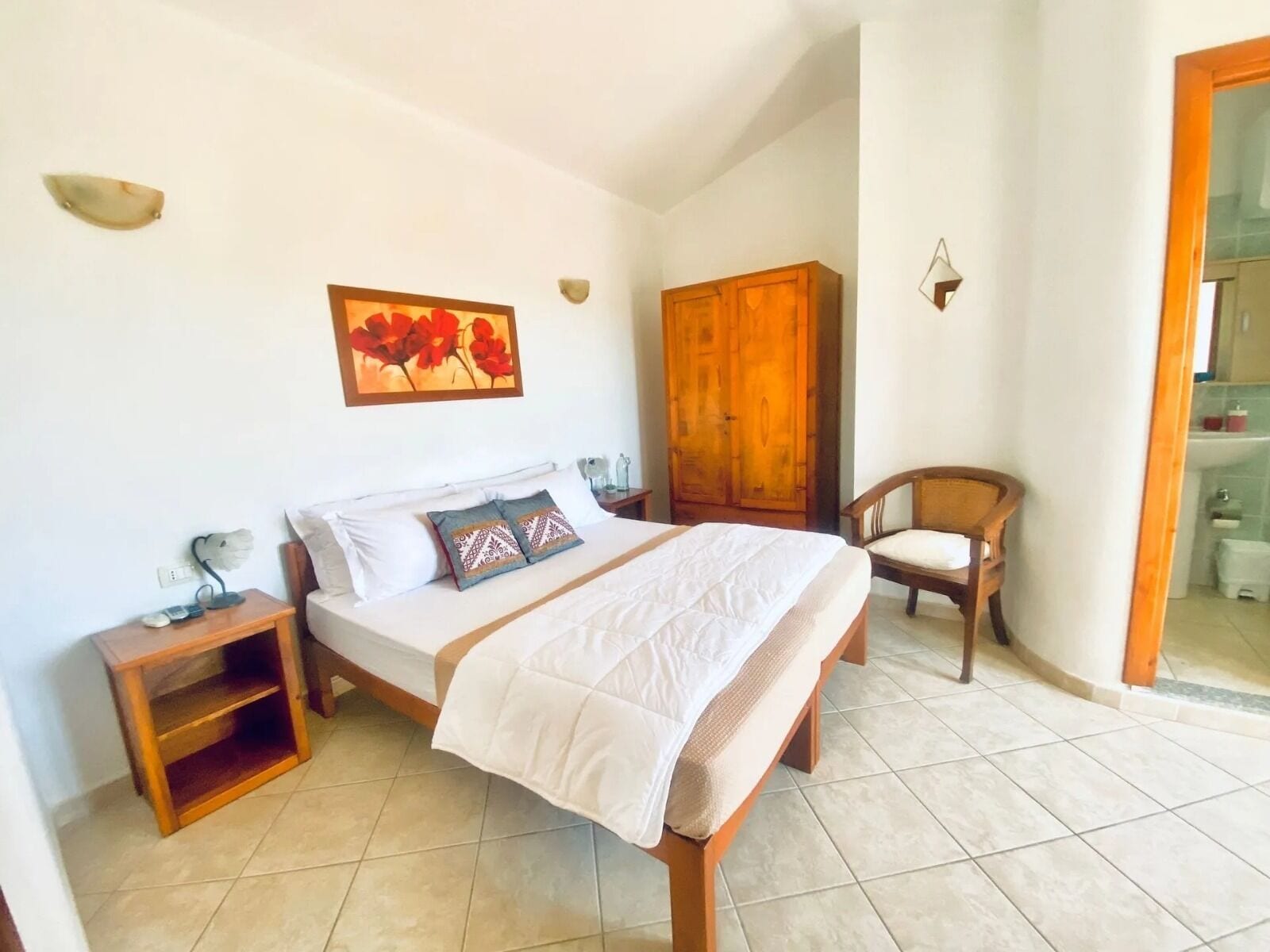 Un dormitorio con cama, mesita de noche, silla, armario y un cuadro en la pared.