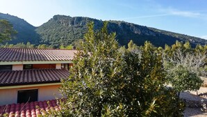 A building with a red-tiled roof, surrounded by greenery and mountains in the background. - Hotel VelaSole (Siniscola)