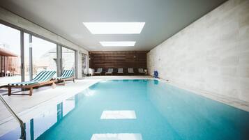 An indoor swimming pool with lounge chairs, large windows, and a wooden wall.