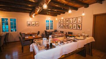 A dining area with a buffet setup, wooden ceiling beams, and framed botanical prints on the wall.