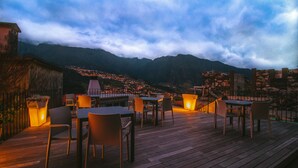 A wooden deck with tables and chairs, overlooking a town and mountains. - Solar da Bica (São Vicente)