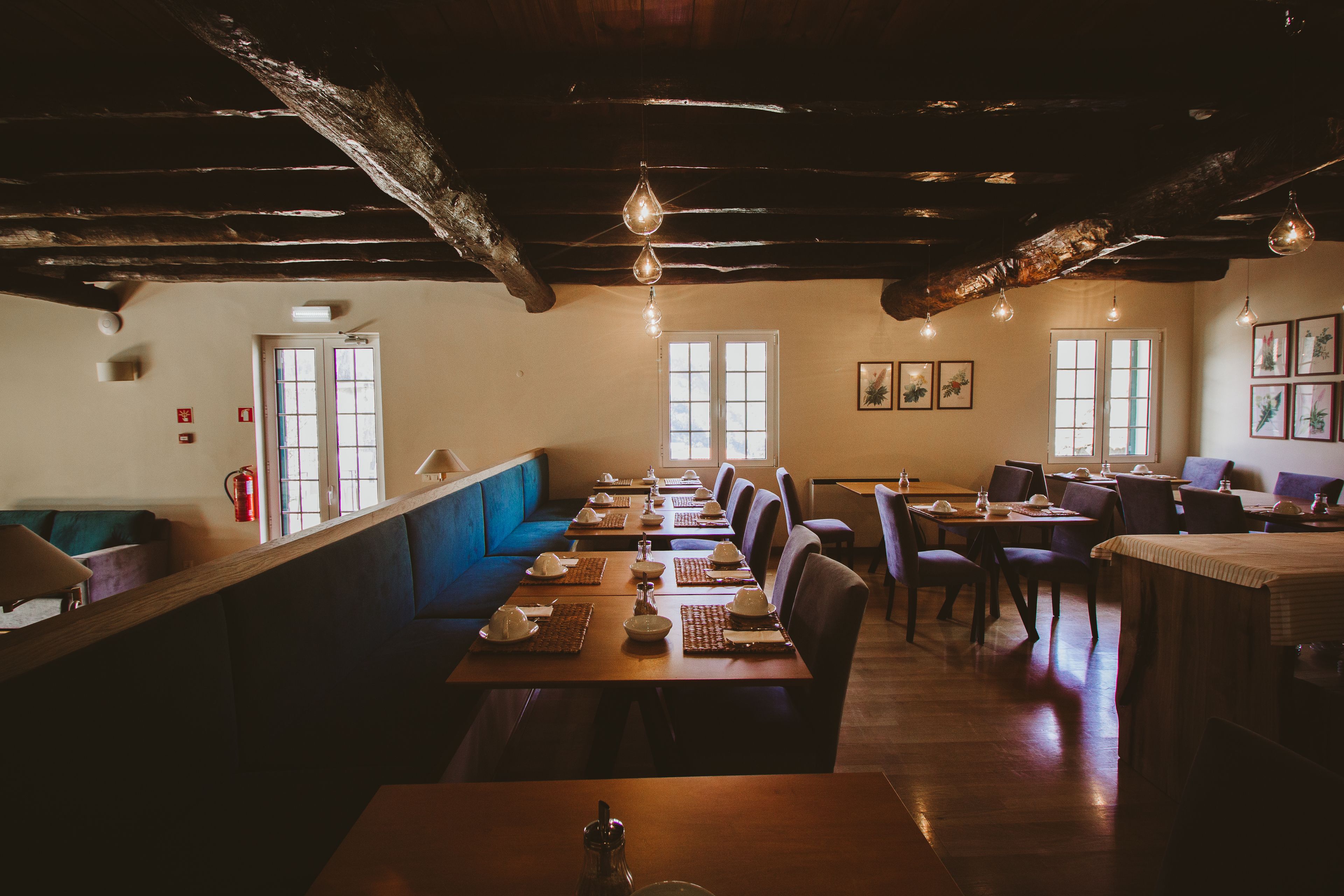 A restaurant with wooden tables and benches, large windows, and hanging light fixtures.