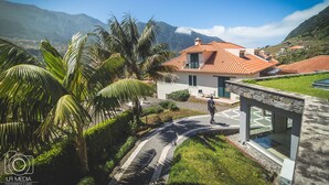 Una casa moderna con techo de tejas, rodeada de abundante vegetación y un paisaje montañoso.