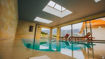 An indoor swimming pool with clear glass walls and a view of a mountain landscape.