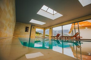 Una piscina interior con paredes de vidrio transparente y vistas a un paisaje montañoso.