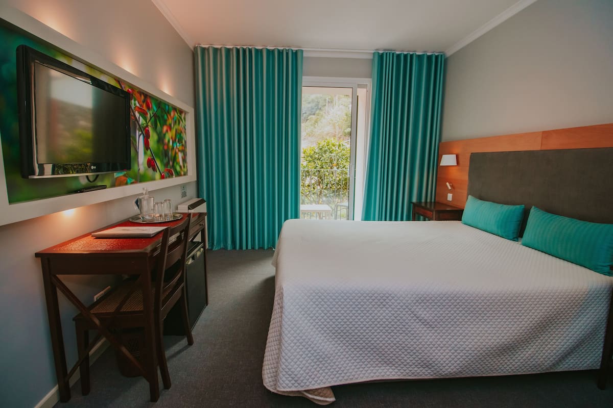 A hotel room with a bed, a desk, a television, and a window with curtains.