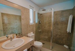Un baño moderno con un espejo grande, un lavamanos, un inodoro y una zona de ducha con mampara de vidrio.
