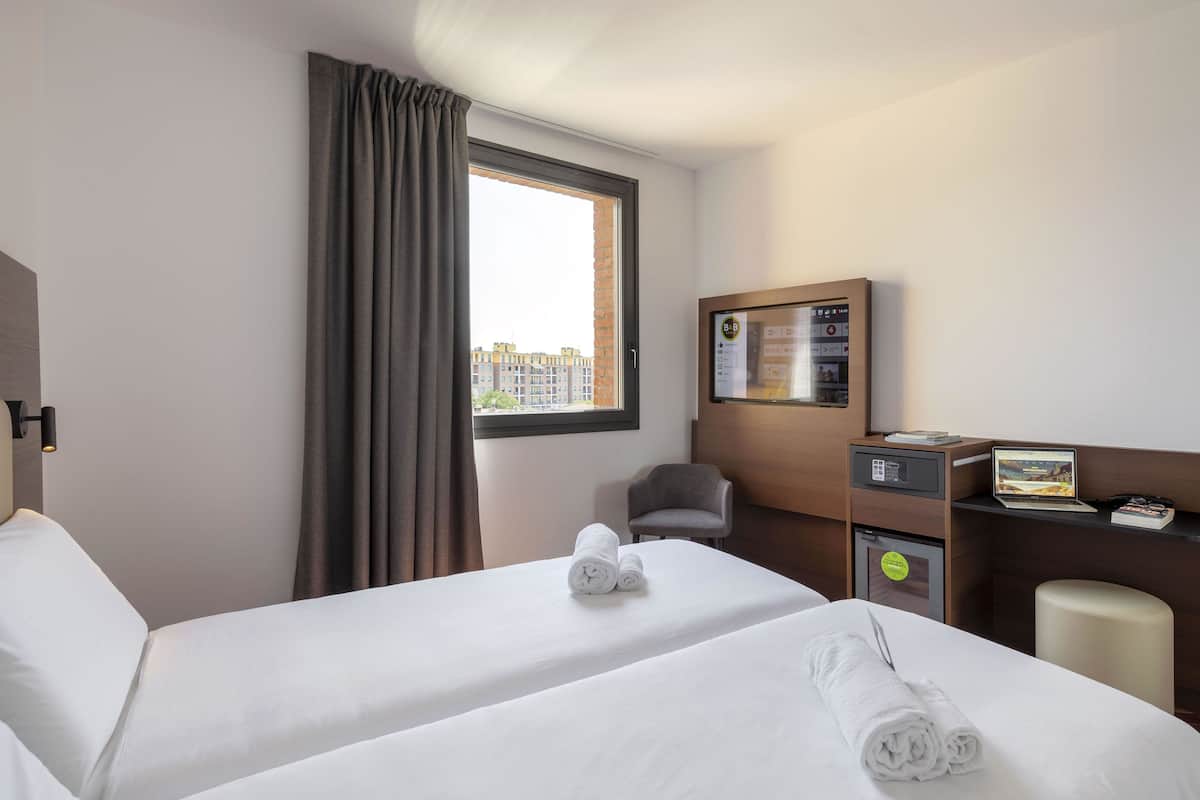 A hotel room with two beds, a desk with a computer, a chair, and a small refrigerator.