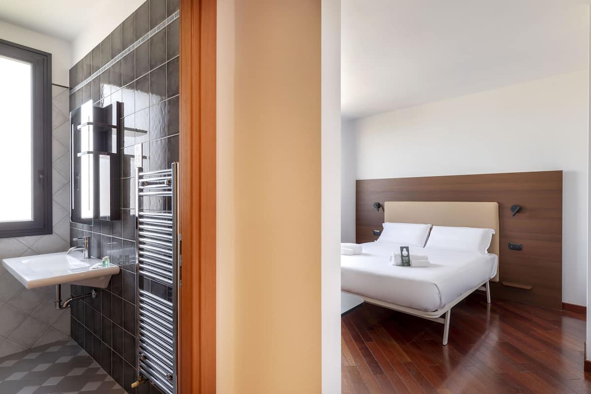 A modern bathroom with a sink, towel rack, and a large mirror. The room has a wooden floor and a window.