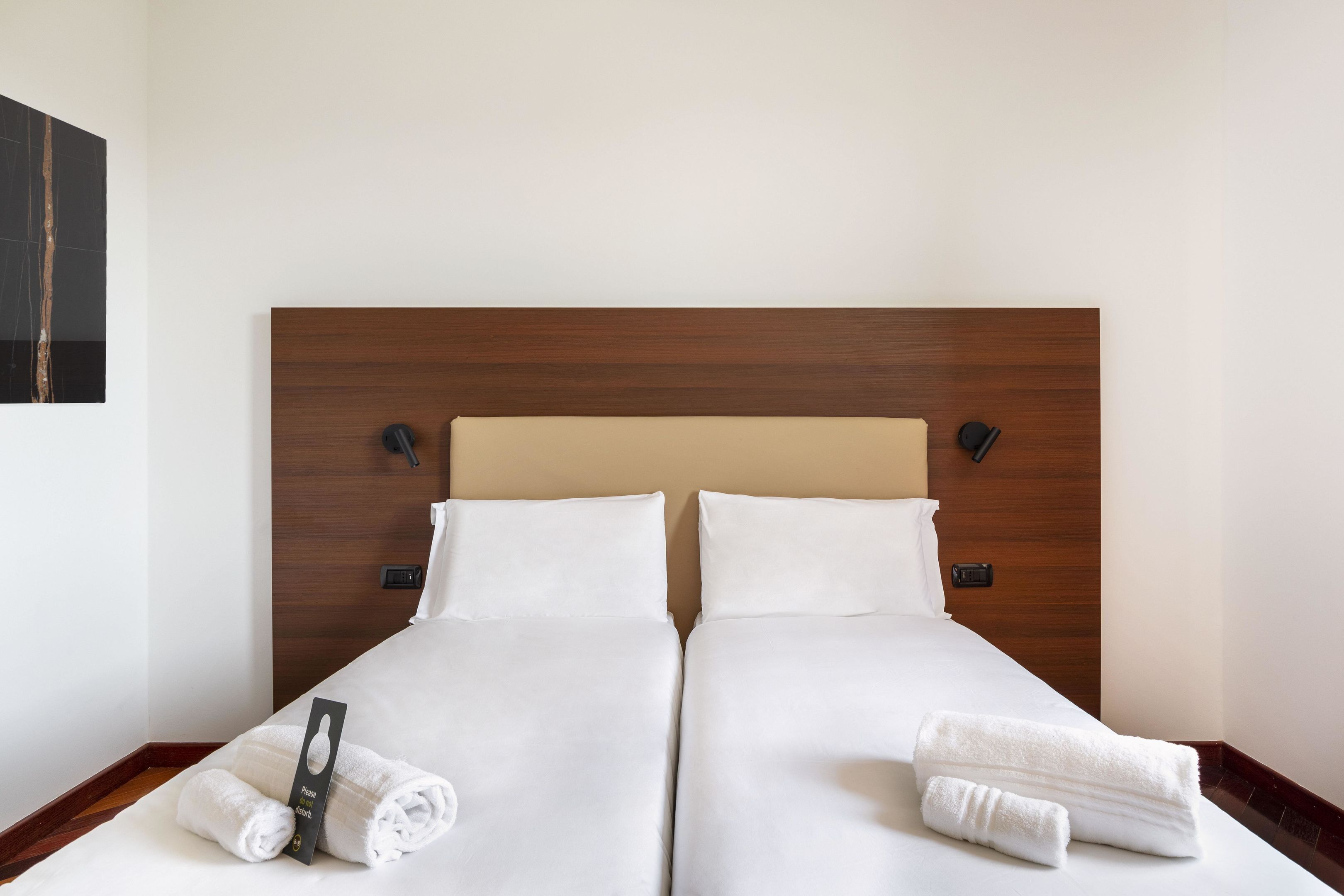 Een tweepersoonsbed met witte lakens en twee opgerolde handdoeken aan weerszijden.