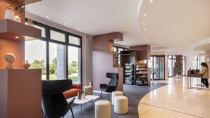 A modern lobby with a curved ceiling, large windows, a reception desk, seating area, and a bookshelf. - B&B Hotel Sassuolo (Sassuolo)