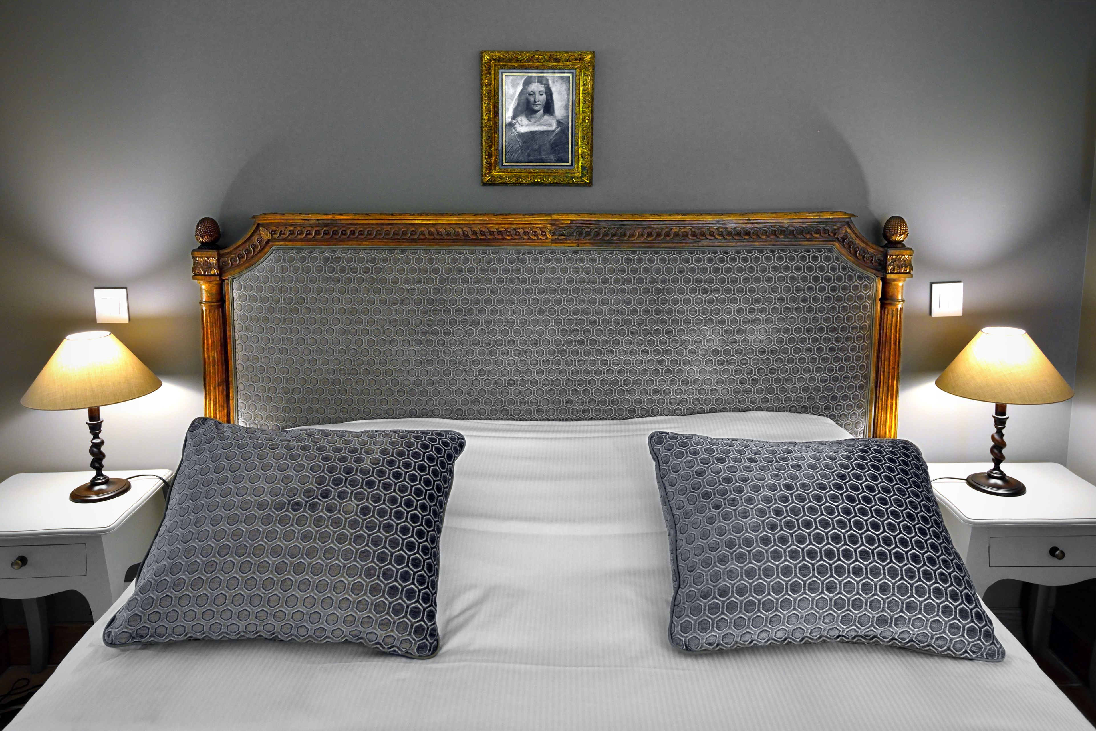Una cama bien hecha con un cabecero estampado, dos almohadas a juego y dos lámparas de noche sobre mesitas blancas.