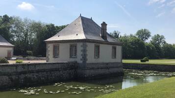 A small, stone building with a gabled roof, situated next to a calm water body with lily pads.