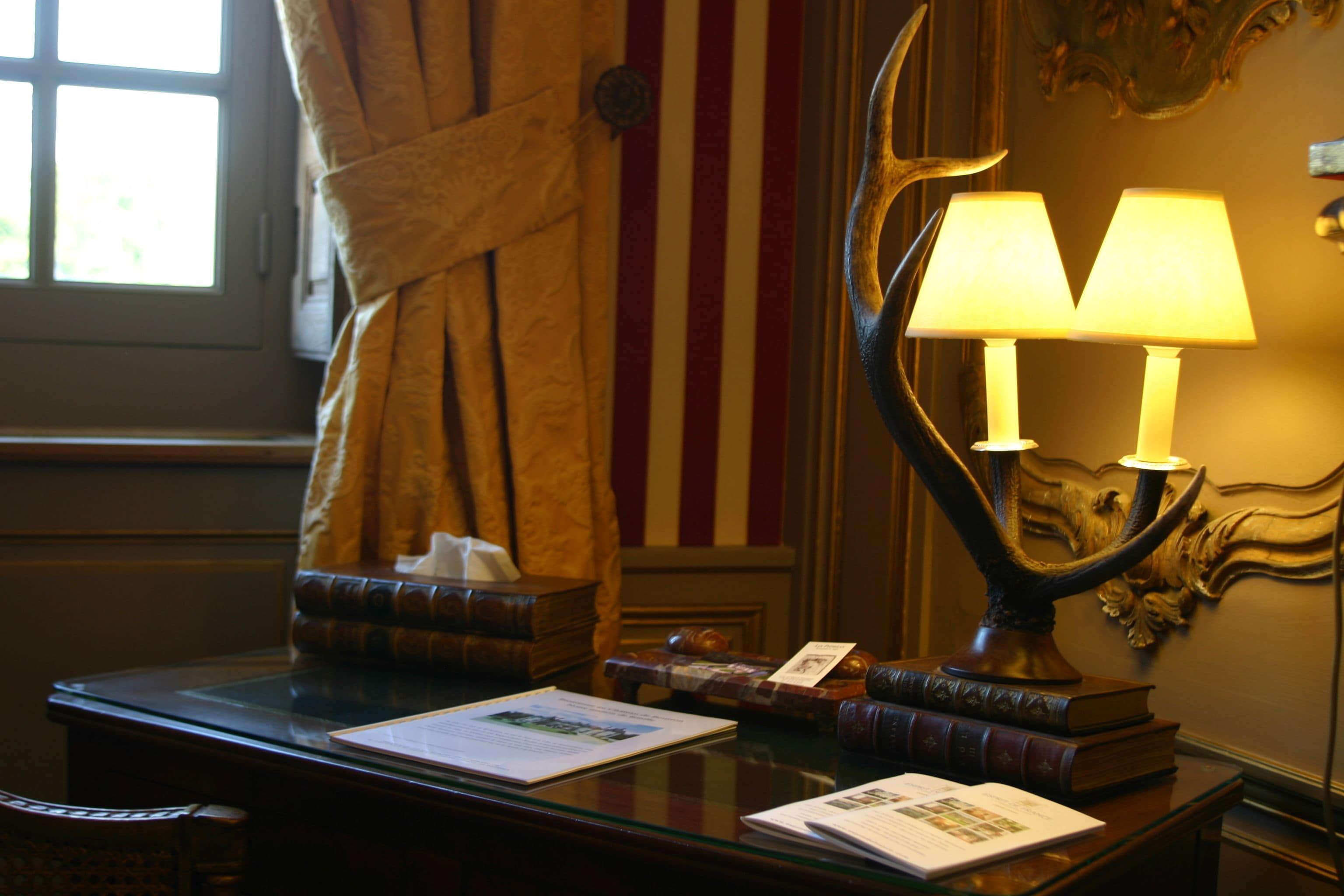 Una habitación con escritorio, libros, lámpara, una bandera estadounidense y una cortina.