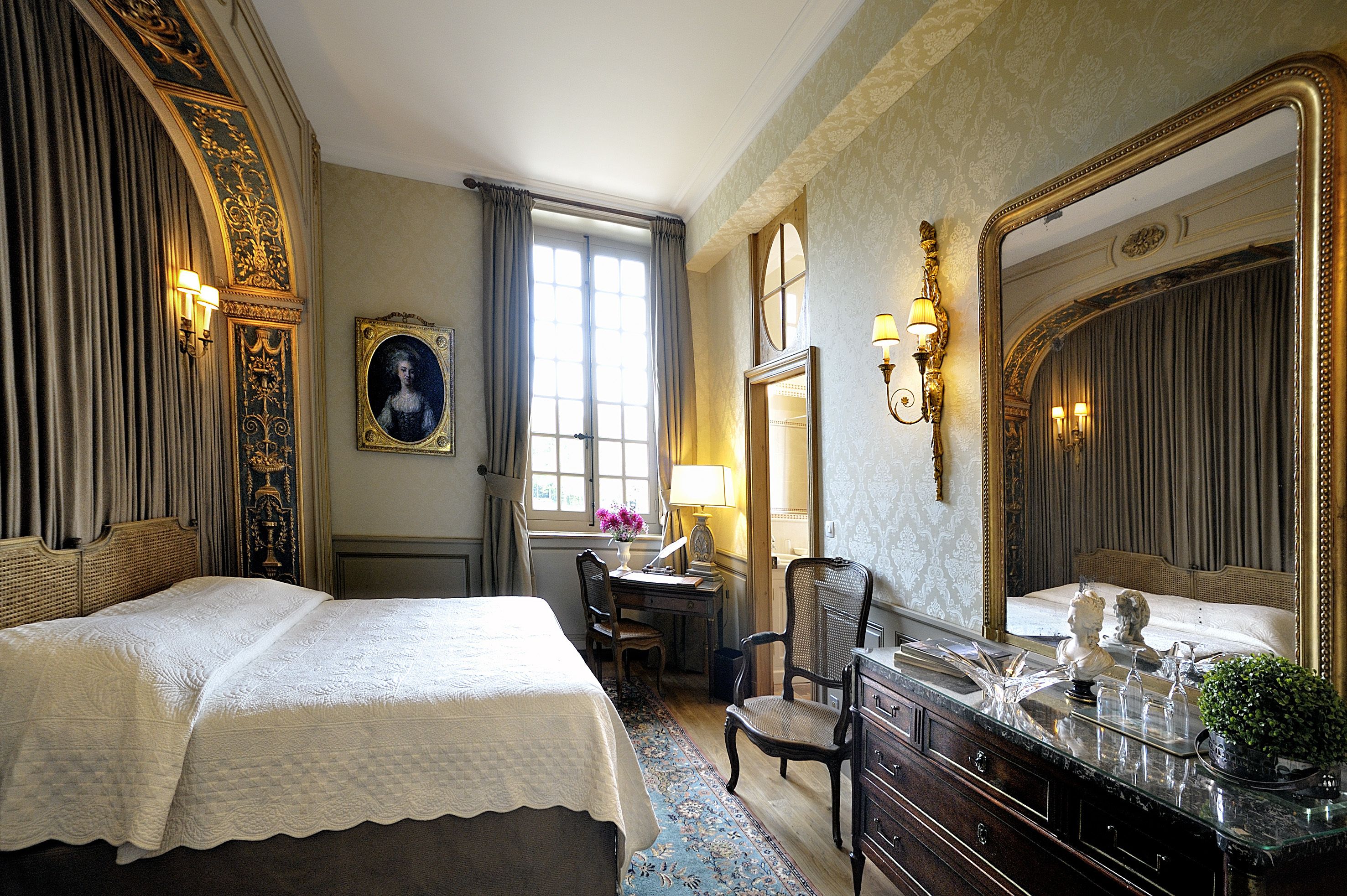 A hotel room with a large bed, a desk with a chair, a dresser, and a large mirror.
