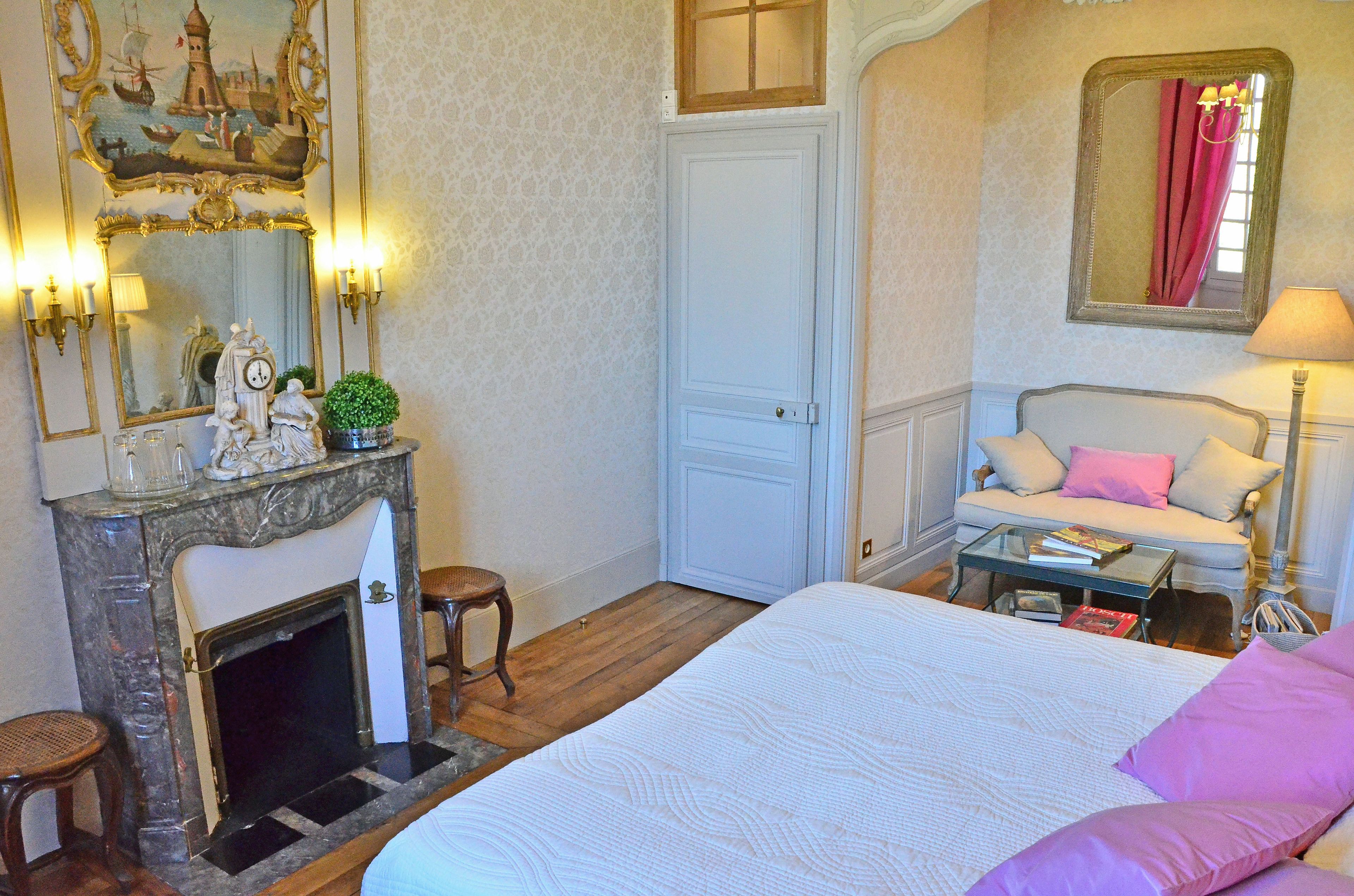 Un dormitorio con cama, sofá, mesita, chimenea y espejo.