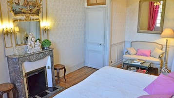 Un dormitorio con cama, sofá, mesita, chimenea y espejo.