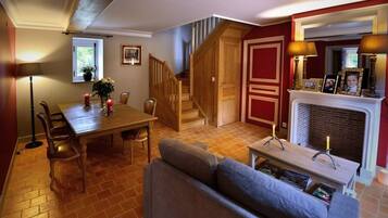 A cozy living room with a fireplace, a dining table with chairs, a sofa, and a staircase leading to another level.