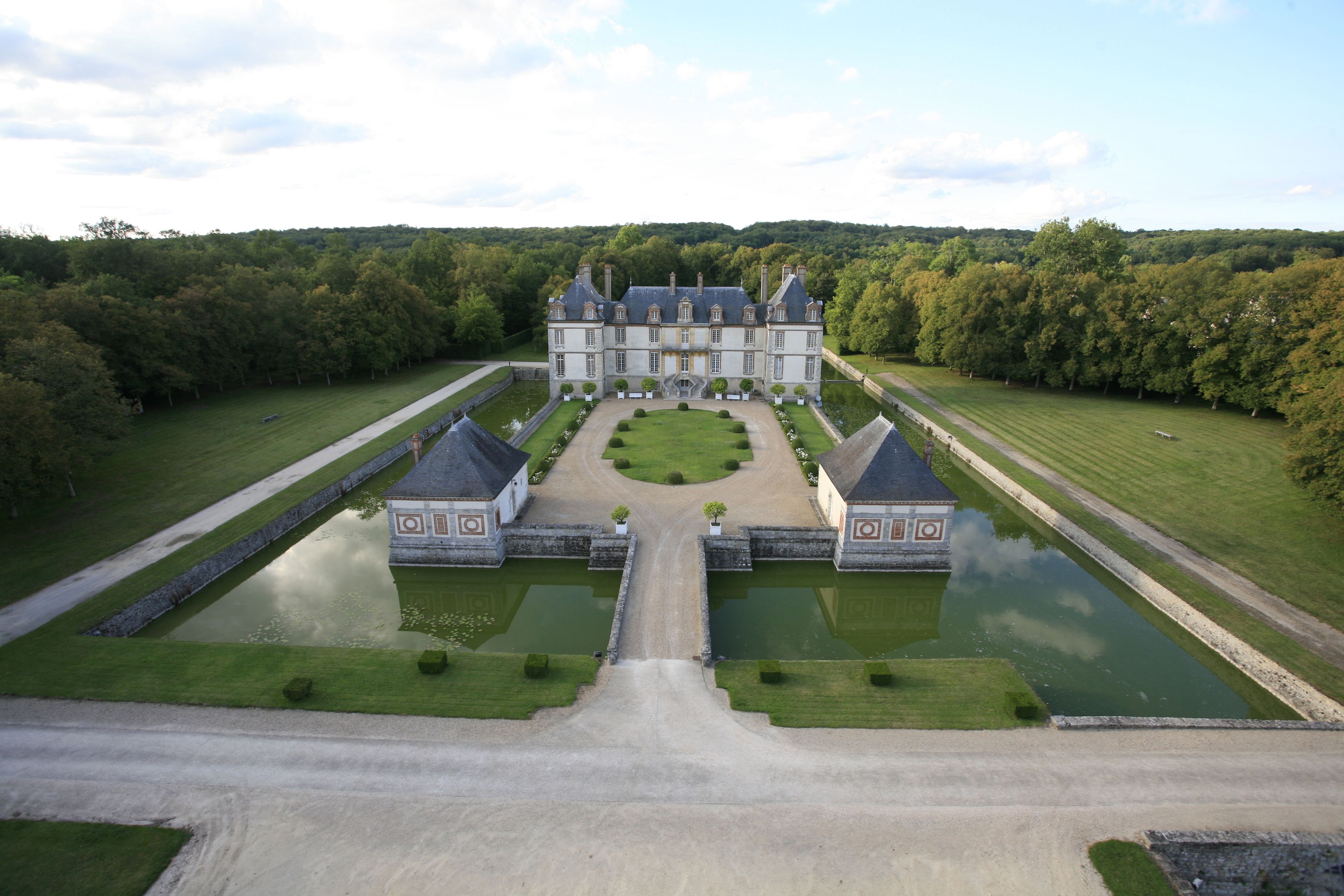 A large, symmetrical building with a central courtyard, surrounded by manicured lawns and water features.
