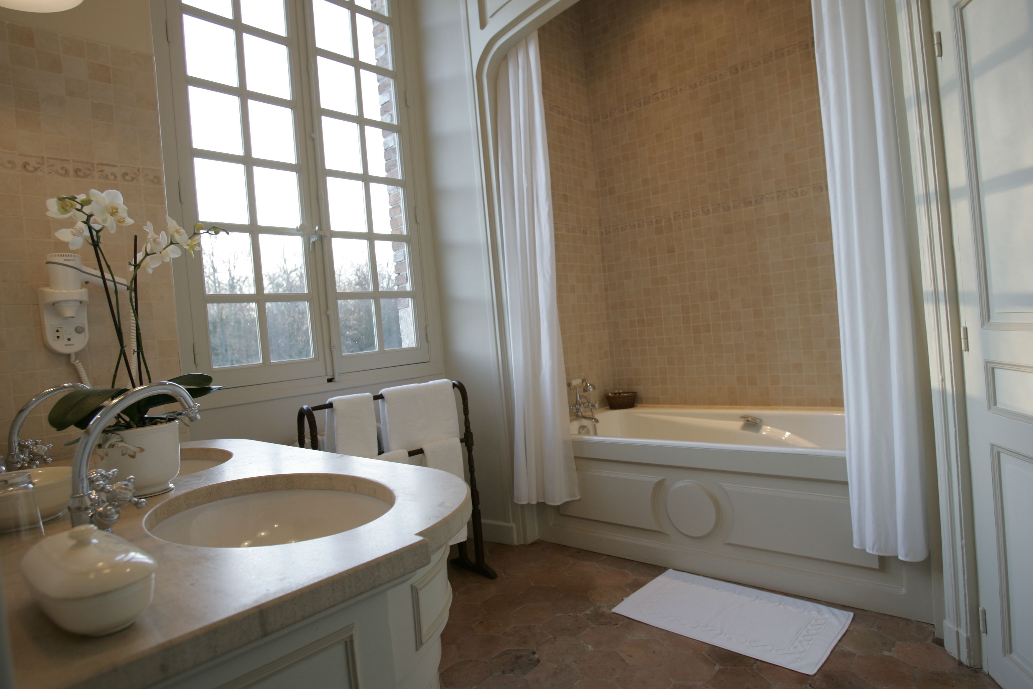 A bathroom with a double sink, a bathtub, and a window with a view of trees.