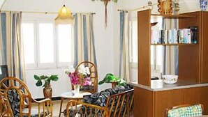 A cozy room with a wooden bookshelf, a dining table with chairs, and a hanging plant. - Villa Veduta (Ghajnsielem)