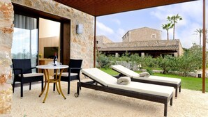 Un espace extérieur aménagé avec une zone de repos couverte, doté d’un mur en pierre, d’une table avec des chaises et de deux fauteuils.