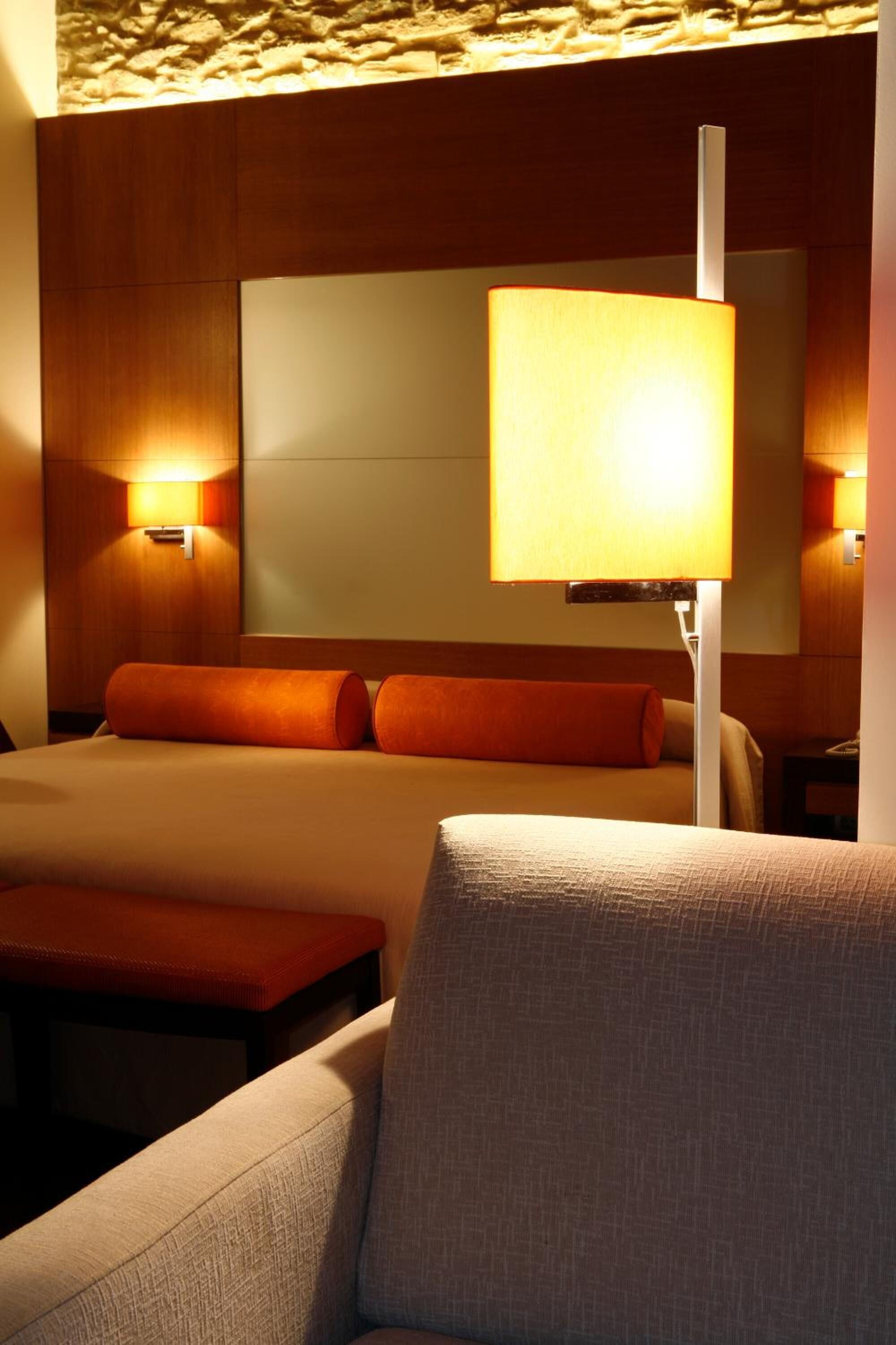 A hotel room with a bed, a nightstand, a lamp, and a chair.