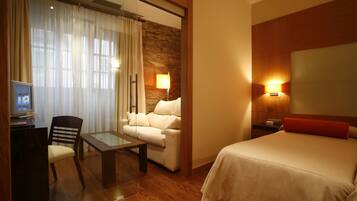 Una habitación de hotel con una cama, un sofá, una mesa de vidrio, un televisor y una lámpara.