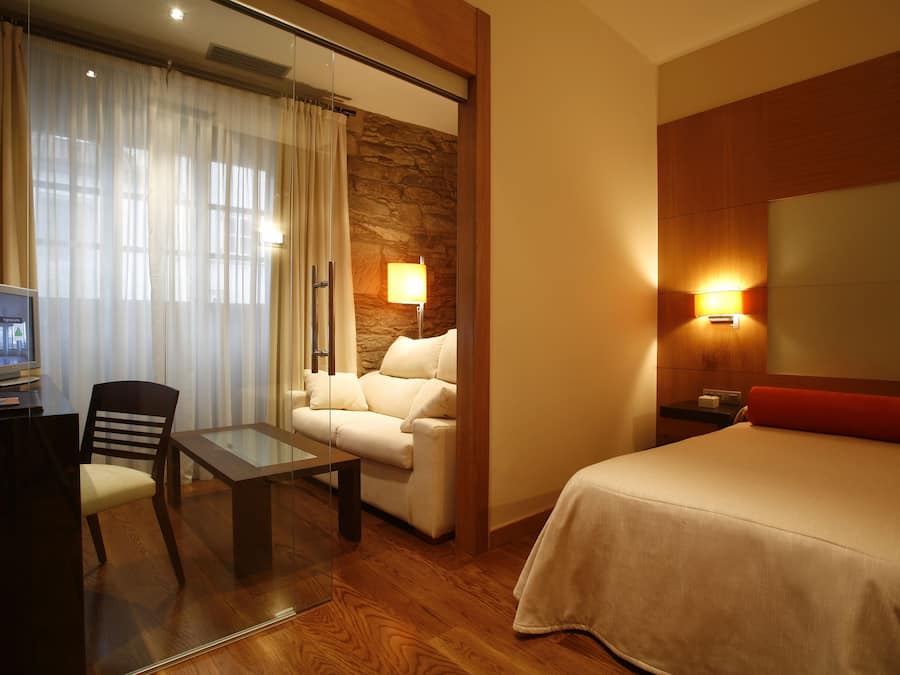 Una habitación de hotel con una cama, un sofá, una mesa de vidrio, un televisor y una lámpara.