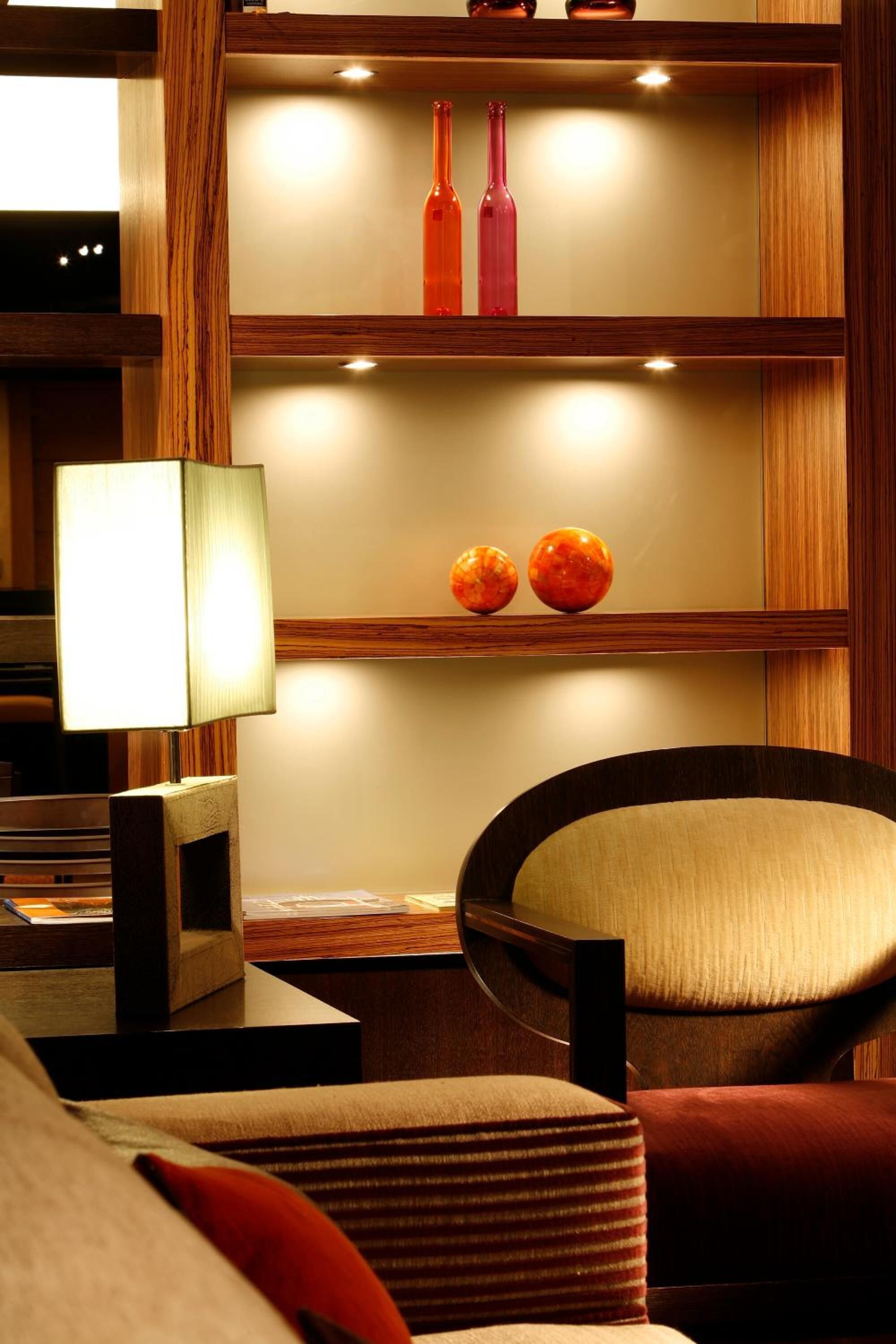 A modern living room with a wooden bookshelf, a lamp, and a comfortable chair.