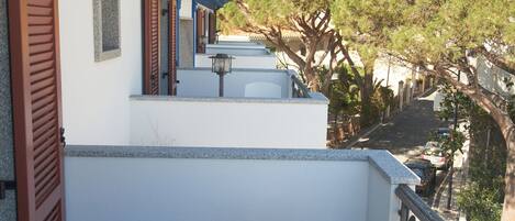 Un balcón con una mesa y sillas blancas, un toldo azul y vistas a un paisaje montañoso.