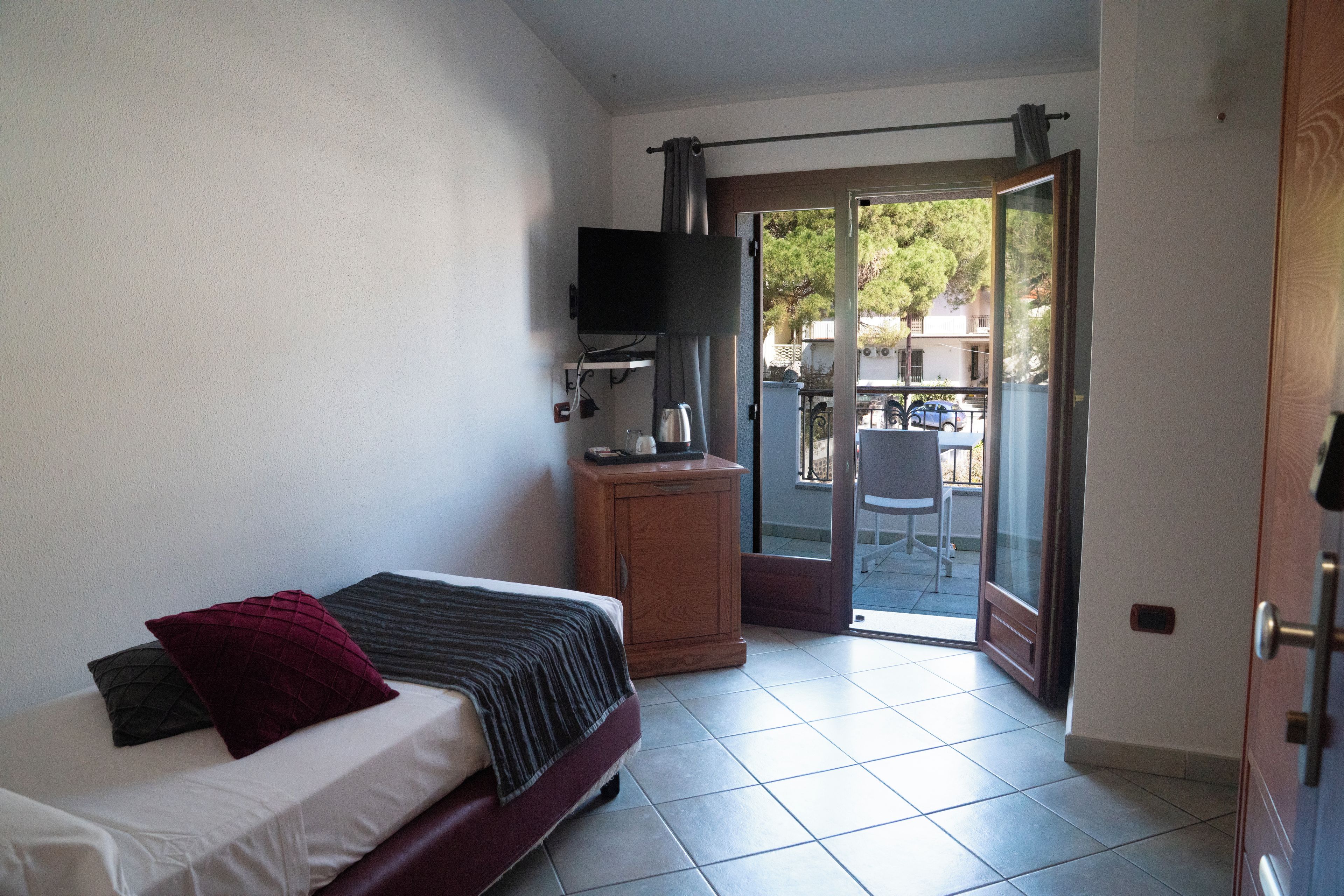 A bedroom with a bed, a television mounted on the wall, and a sliding glass door leading to an outdoor area.