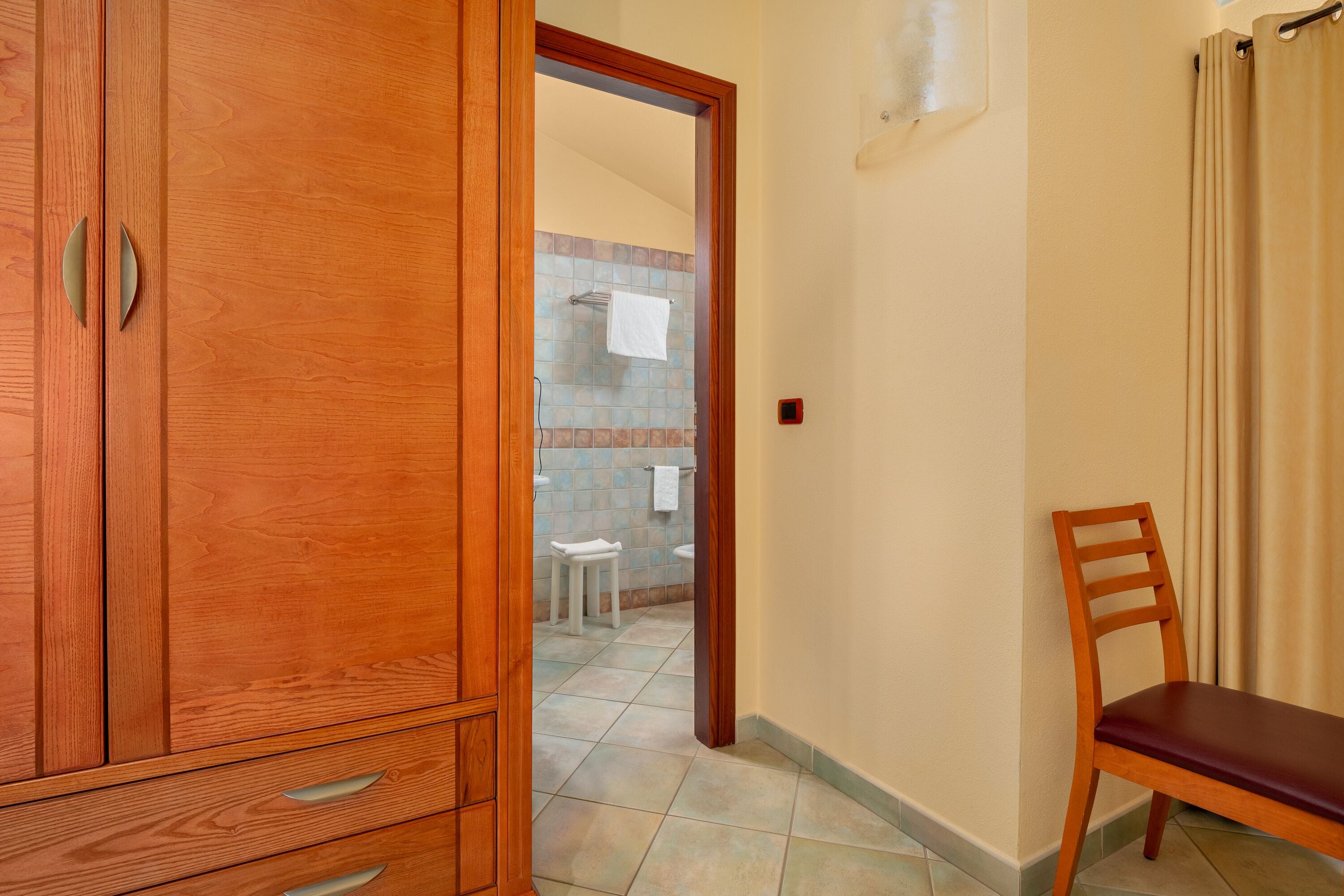 A wooden wardrobe with drawers, a wooden chair, and a tiled floor.