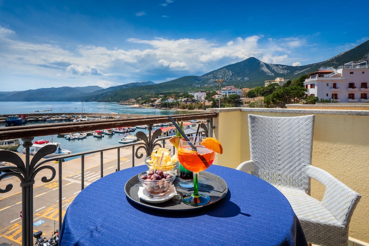 A balcony with a table set for two, overlooking a marina and a mountainous landscape.