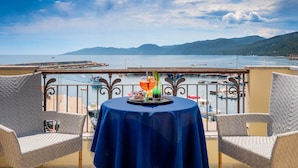 Un balcón con una mesa lista para dos personas, con vistas a un puerto deportivo con barcos y montañas al fondo.