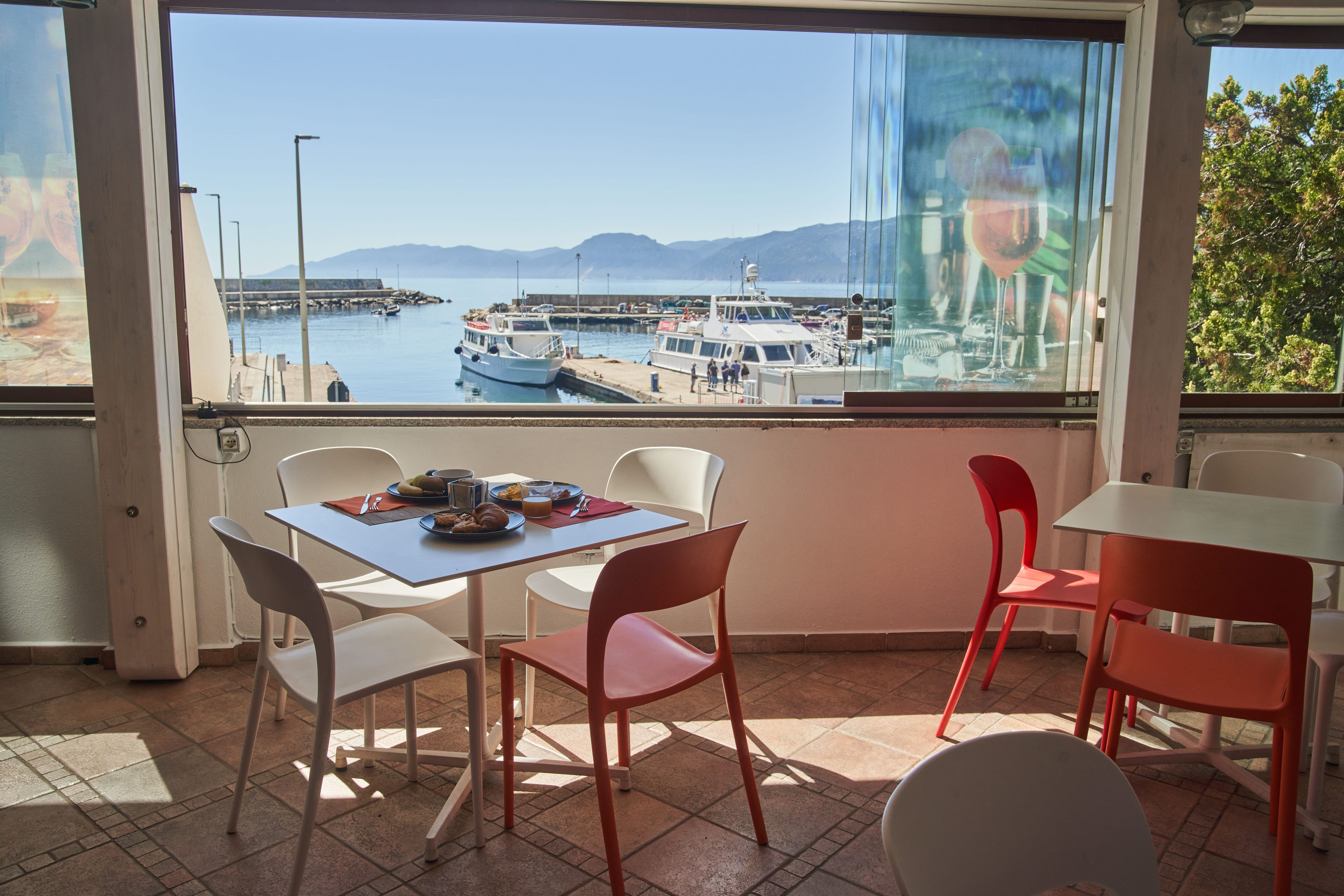 A dining area with a table and chairs, a view of boats at a marina, and a glass door reflecting the scene.