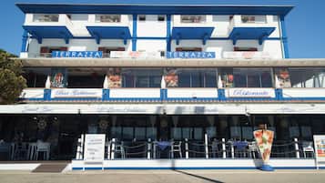 Un restaurant situé au bord de l’eau, avec une terrasse et proposant différents types de repas, notamment un bar et une pizzeria.