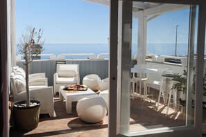 Un área de estar al aire libre con muebles blancos, una mesa de comedor con comida y vistas al mar.