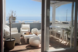 Un área de estar al aire libre con muebles blancos, una mesa de comedor con comida y vistas al mar.