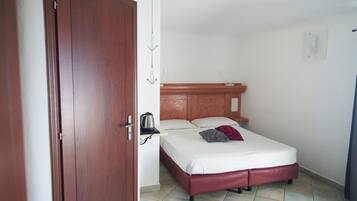 Un dormitorio con puerta de madera, cama con cabecero y mesita de noche con tetera.
