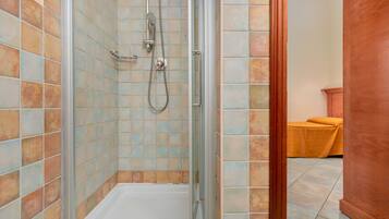 A shower area with a glass door, tiled walls, and a wooden bench in the background.