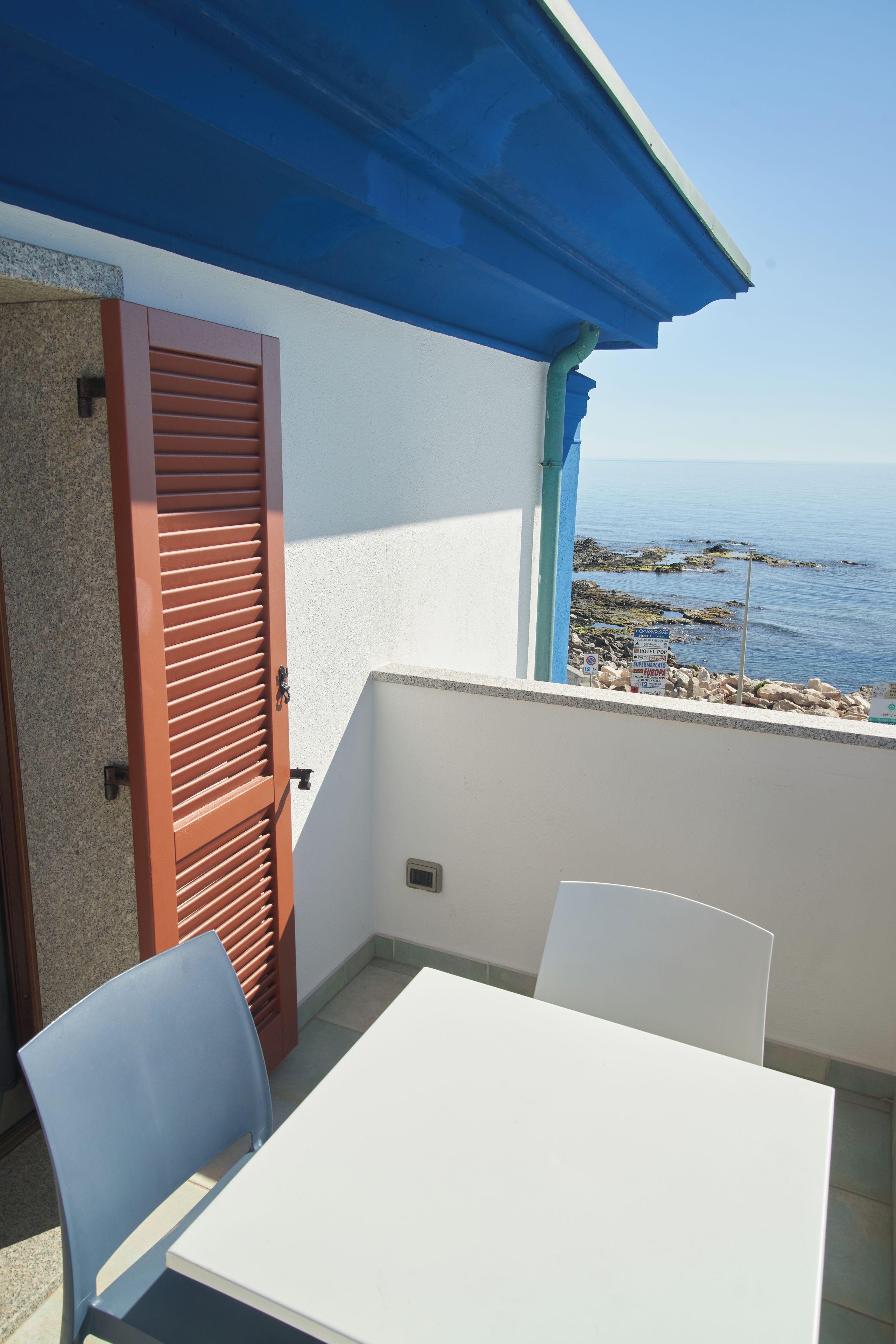 Un balcón con una mesa y sillas blancas, un toldo azul y vista al mar.