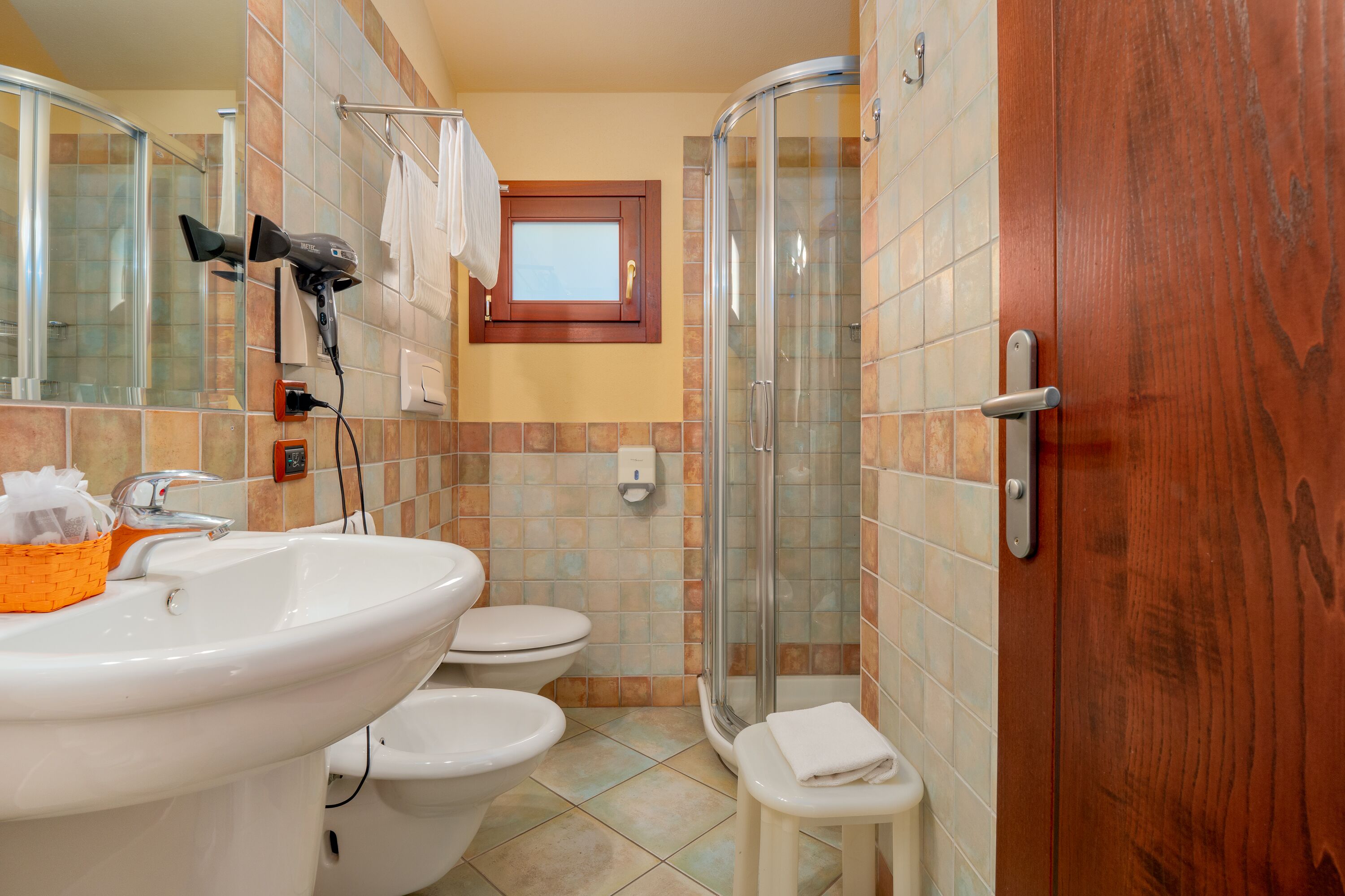A bathroom with a sink, two toilets, a glass shower enclosure, and a towel rack.