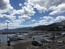A marina with boats docked, a parking area with cars, and a mountainous backdrop.