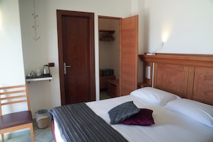 A hotel room with a bed, a chair, a desk with a kettle, and a wardrobe.